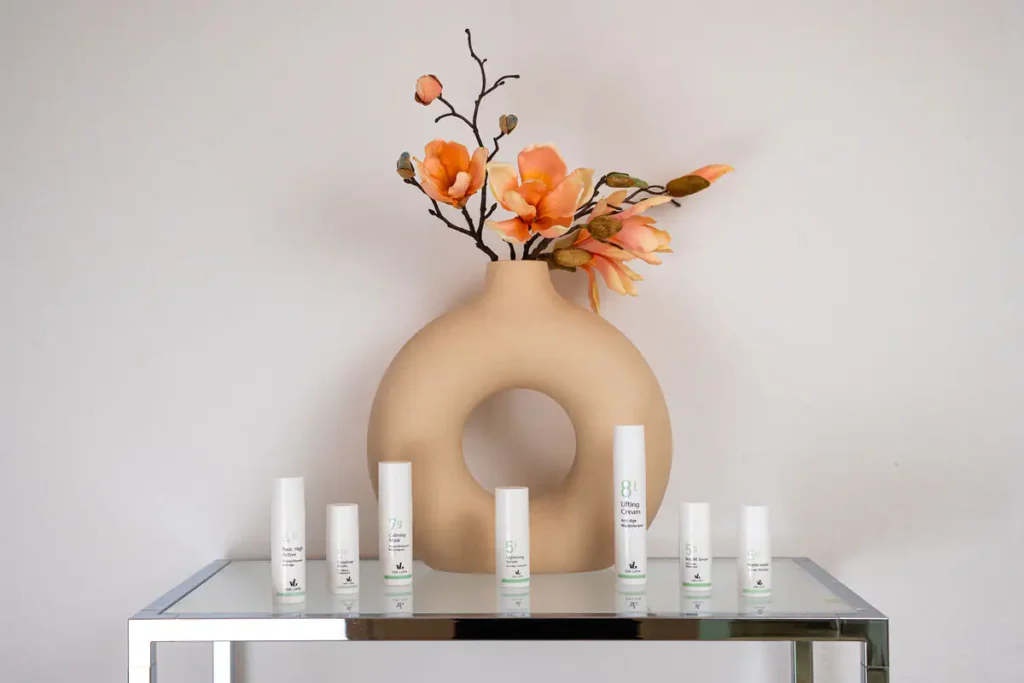 Pflegeprodukte von VON LUPIN auf einem Glastisch vor einer Vase mit Magnolienzweig